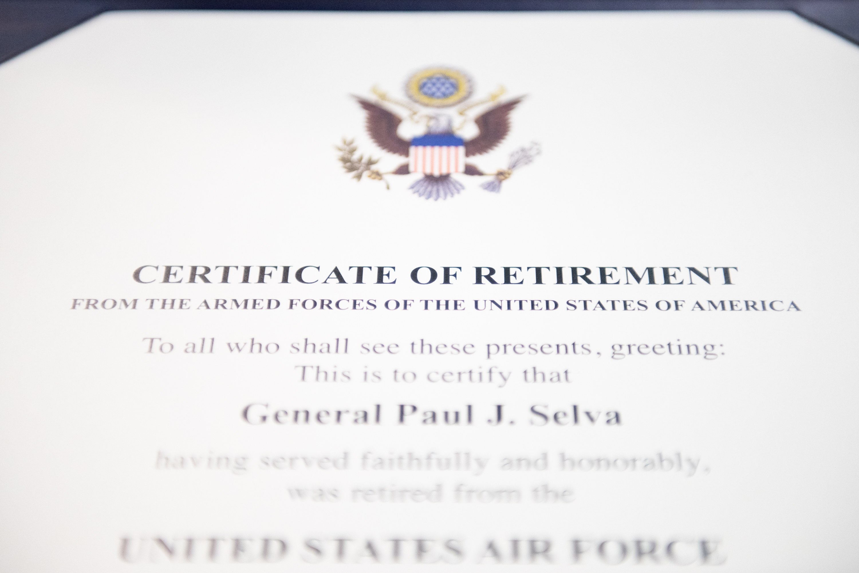 Framed certificate of retirement from the United States Air Force with a blue border, featuring a central star shield logo within a laurel wreath and a "Retirement" banner, all printed in black ink.