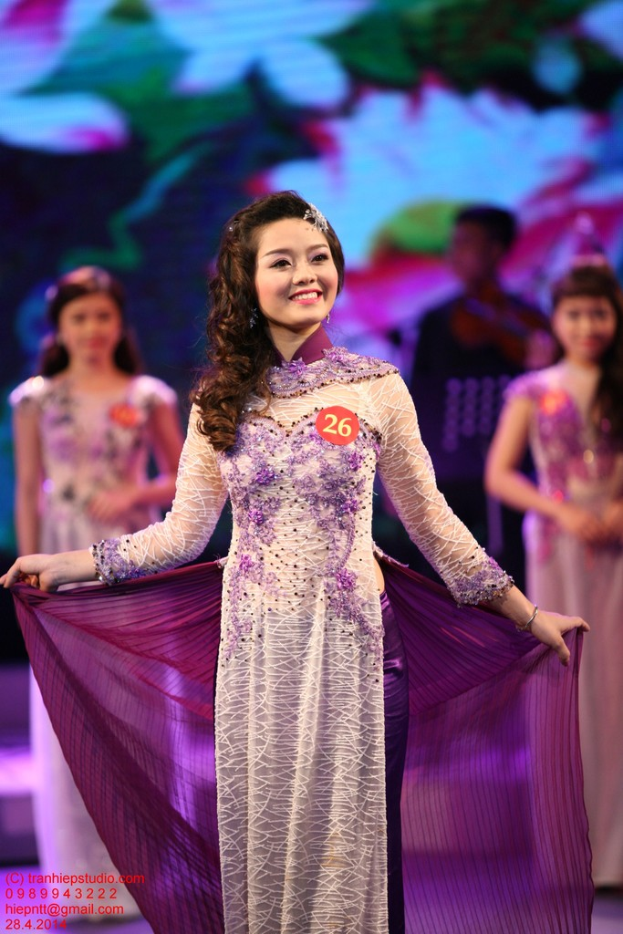 Eine Frau in einem creme- und lilafarbenen Kleid mit einem Anstecker darauf, mit einem unscharfen Hintergrund.