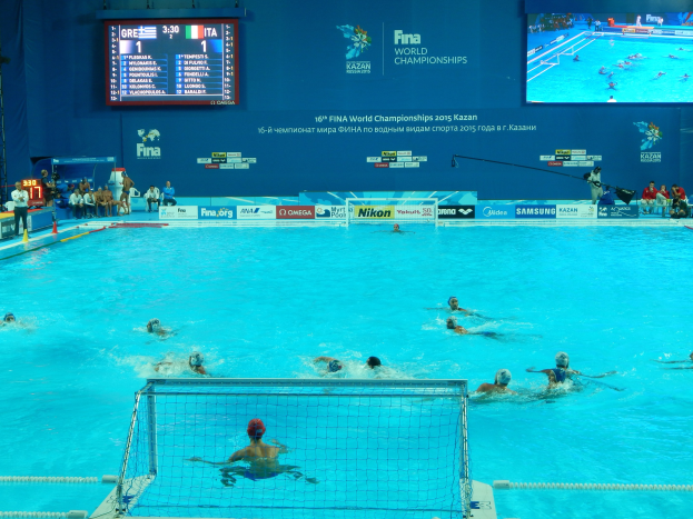 Gruppe von Menschen, die Wasserball spielen in einem Pool während der 2016 FINA Weltmeisterschaft in Kazan, mit einem Netz, das den Pool trennt und Zuschauern auf der linken Seite sitzen.