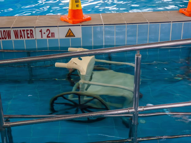 Schwimmbad mit einem Stuhl in der Mitte, umgeben von Sicherheitskegeln und einem Geländer, und einem Schild an der Wand, das verfügbare Schwimmausrüstung anzeigt.