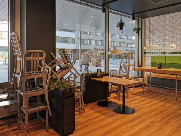 Ein Restaurant mit Holztischen und -stühlen, die durch ein großes Fenster zu sehen sind, das in Berlin, Deutschland, liegt, mit Menschen, die auf der Straße gehen.