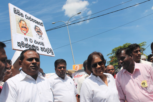 Männer stehen und protestieren mit Schildern, Stangen, Drähten, Bäumen und dem Himmel im Hintergrund.