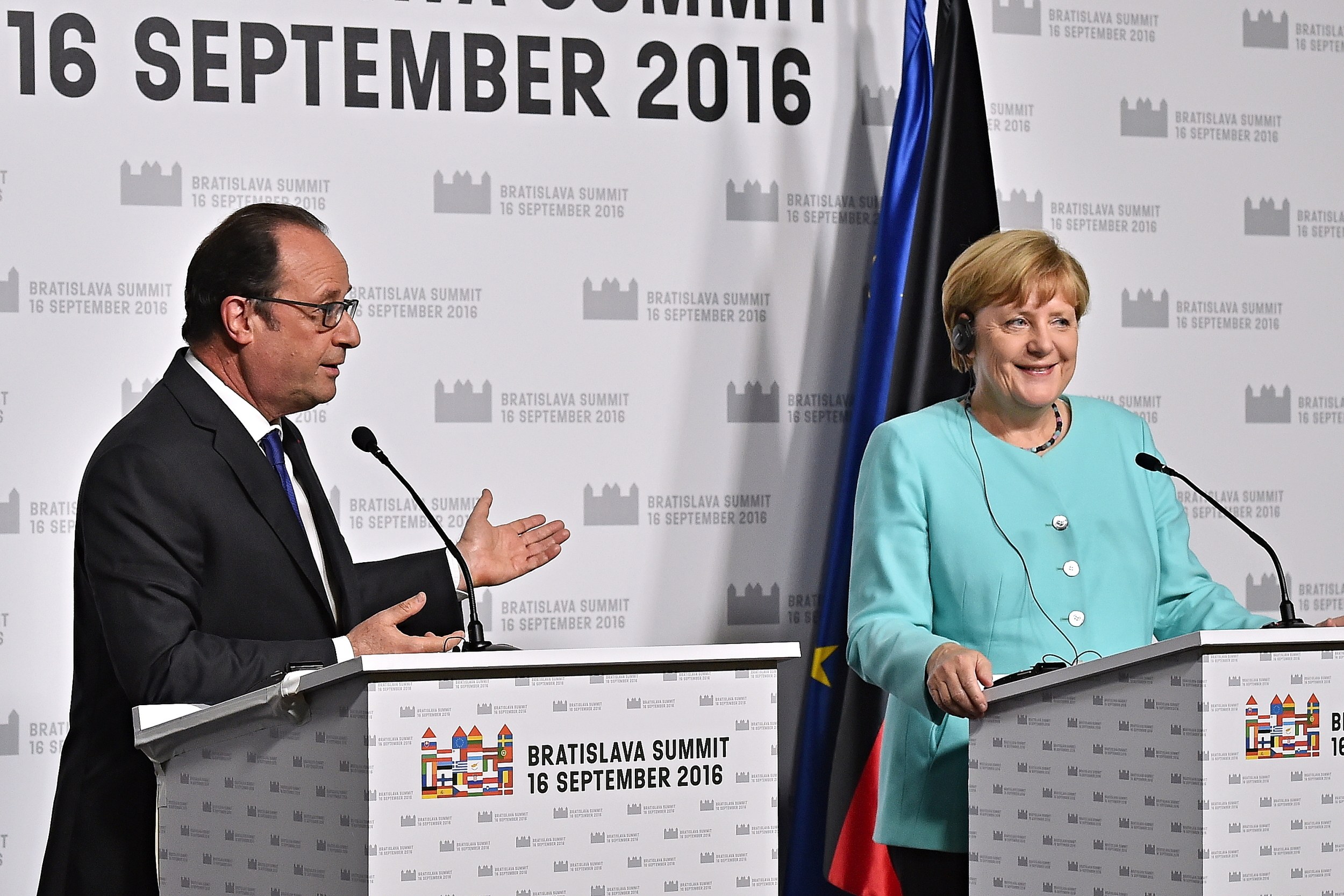 Two smiling leaders, Angela Merkel and François Hollande, stand at podiums with microphones, in front of a "Bratislava Summit 2016" banner.