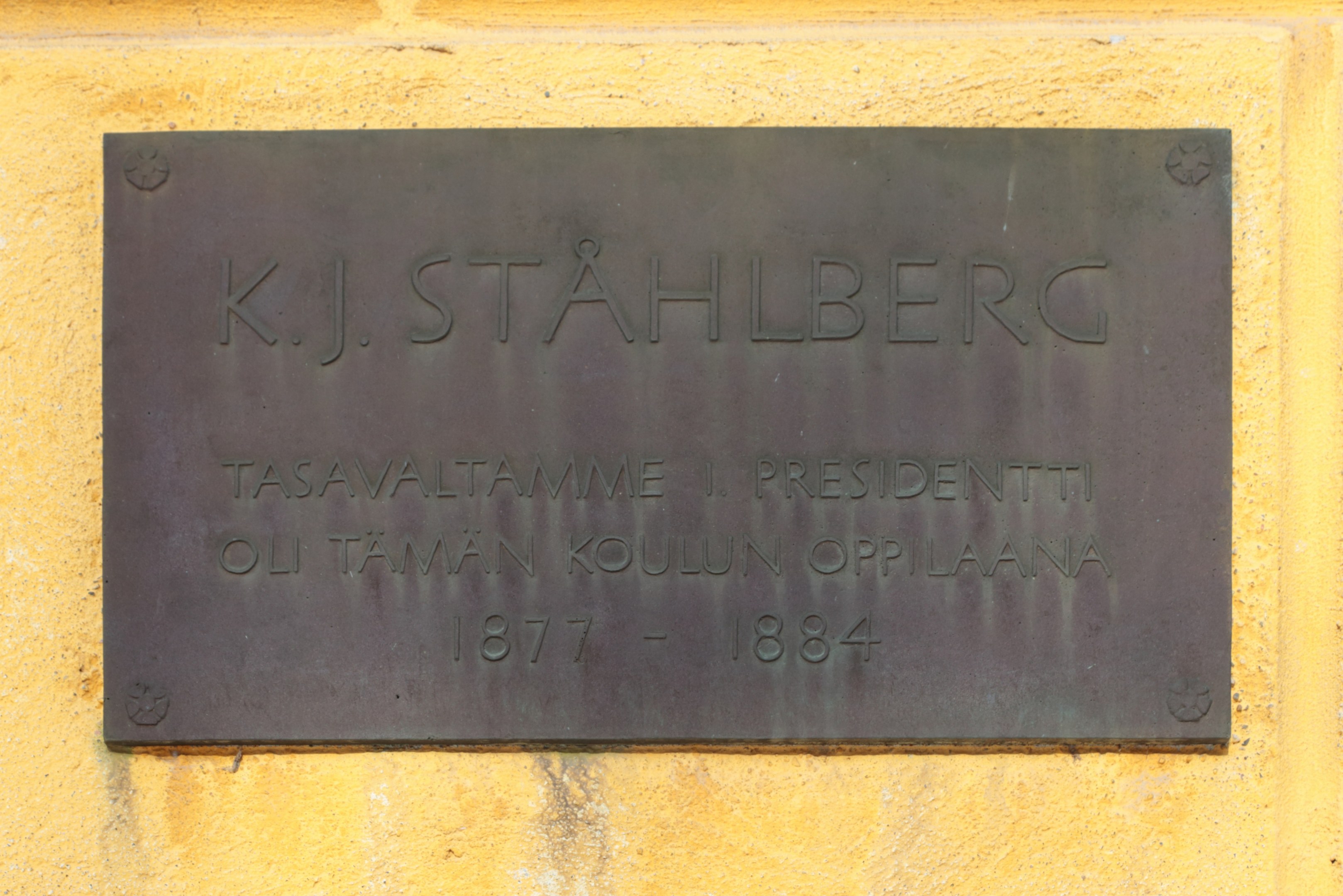 A yellow wall with a metal plaque inscribed "K.J. Stahlberg".