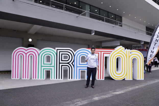 Ein Mann, der vor einem "Marathon"-Schild strahlt, umgeben von Menschen mit Schildern und einem beleuchteten Gebäude im Hintergrund.