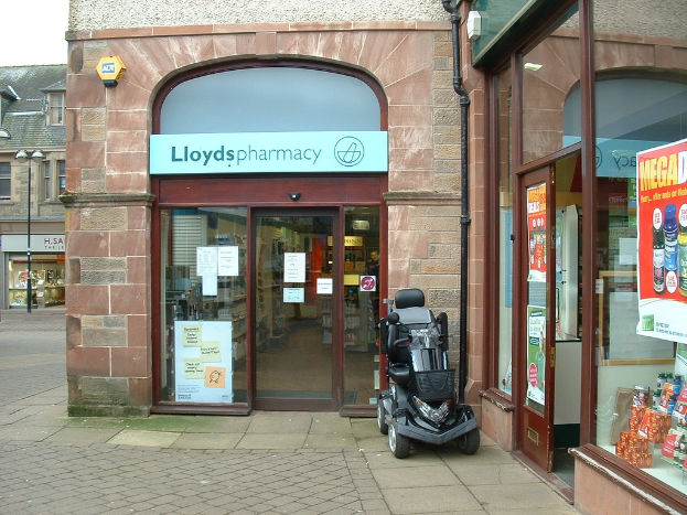 Eine Apotheke mit einem Fahrzeug davor und einem Geb√§ude in der linken Ecke.