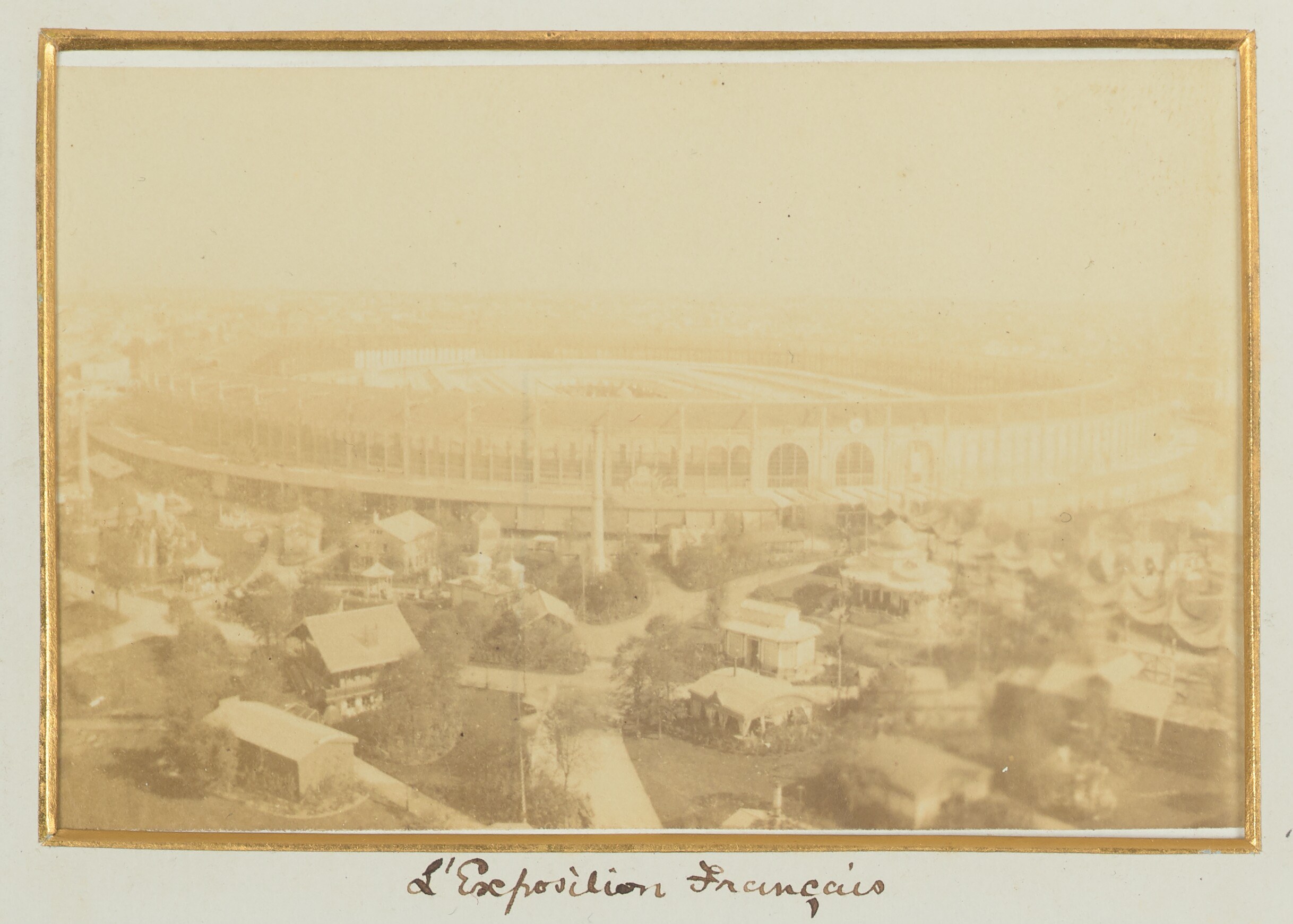 Old black-and-white photo of a stadium surrounded by buildings, trees, and utility poles with text at the bottom.