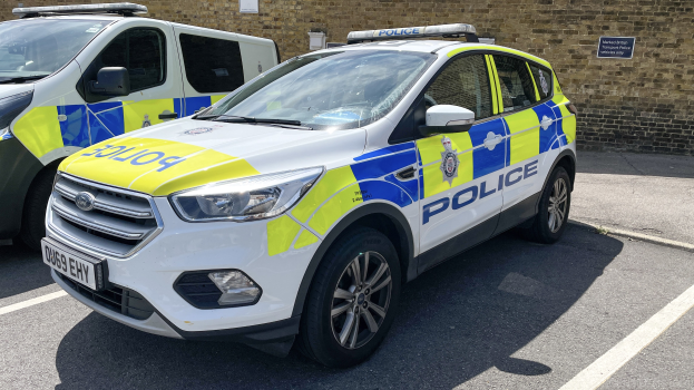 Zwei Polizeiwagen nebeneinander auf einem Parkplatz mit einer Tafel an einer Wand dahinter.