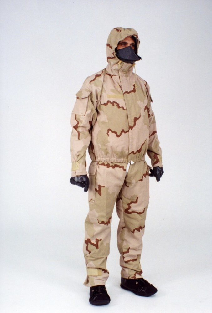 Ein Mann in einem Tarnmuster-Schutzoverall und Maske steht vor einem weißen Hintergrund, der Anzug ist für den Schutz vor gefährlichen Materialien mit einer Kapuze, verstellbaren Riemen und Reißverschluss ausgestattet.