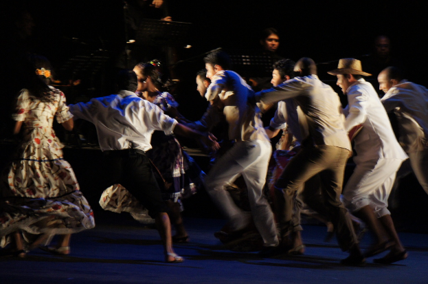 Eine Gruppe von Menschen, die mit anderen und Equipment im Hintergrund auf einem Boden tanzen.
