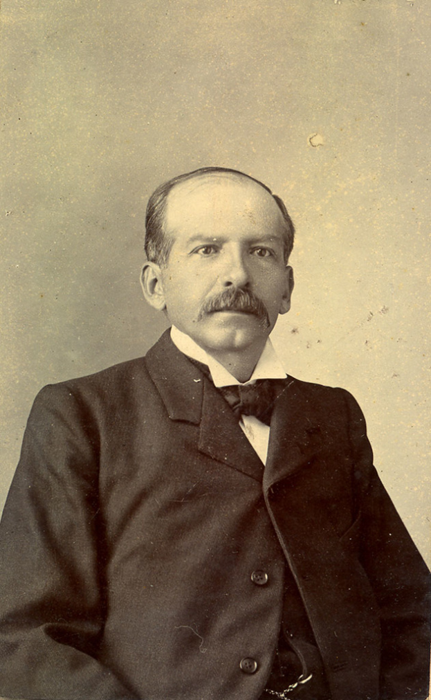 Ein älterer Mann in einem Anzug steht vor einer Wand.