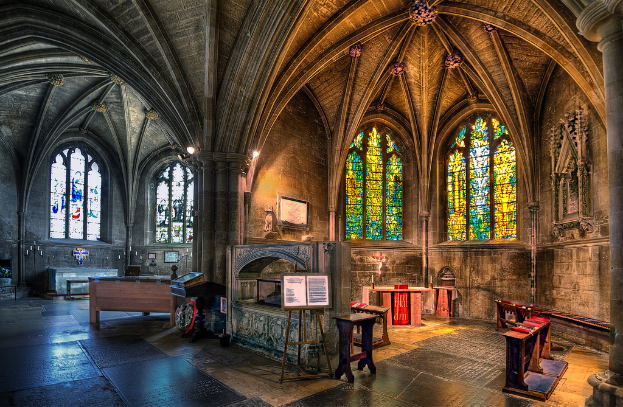 Ein Raum mit Bänken, Tischen, einer Tafel, Fenstern, einer Wand, Kerzen, einem Kamin und Lichtern in der Mitte, bearbeitet.