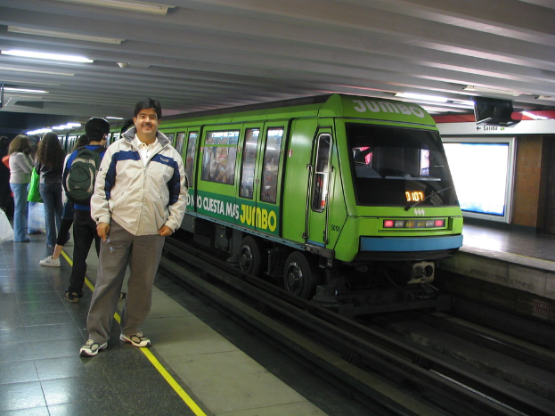 Ein Zug auf einem Bahngleis mit Menschen auf der linken Seite und einem Dach am oberen Rand des Bildes.