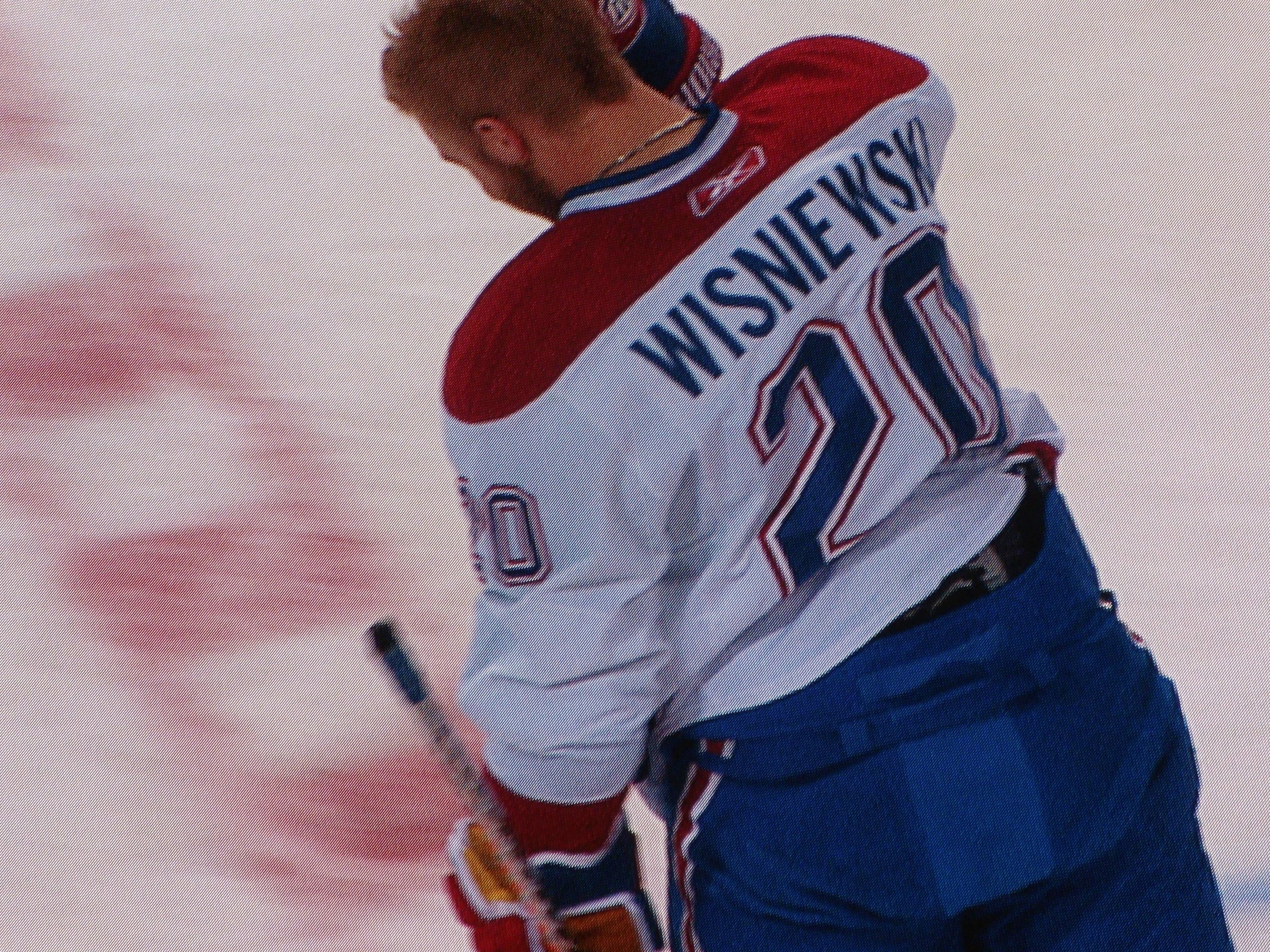 Berufshockeyspieler in einem "Wisniewski"-Trikot auf dem Eis stehend und einen Hockey-Schläger haltend, mit konzentrierter Miene.
