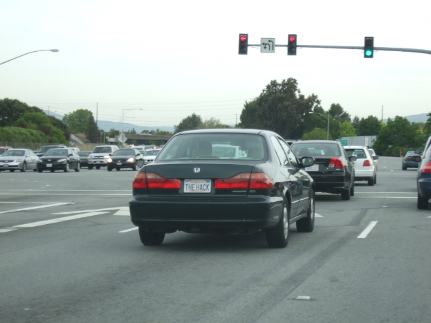 Eine befahrene Straße mit mehreren Fahrzeugen, drei Strommasten und einem Verkehrszeichen auf der rechten Seite bei klarem Himmel.