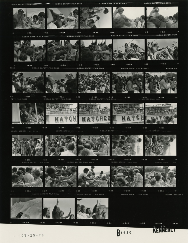 Schwarzes und weißes Foto einer vielseitigen Menge, die fröhlich in Richtung eines Fernsehbildschirms schaut, mit Text unten.