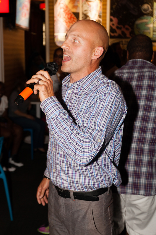 Eine Person in einem schwarzen Gürtel steht und singt in ein Mikrofon, während eine Gruppe von Menschen hinter ihnen steht.