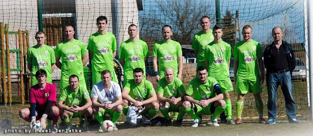Eine Gruppe von Männern in grünen T-Shirts steht auf einem Fußballfeld, einige hocken, mit einem Ball und einem Torpfosten im Bild.
