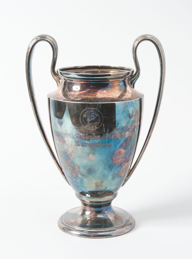 Der UEFA-Champions-League-Pokal, ein stählerner Becher mit zwei Griffen, blau und silbern, mit der Inschrift "UEFA Champions League", vor einem weißen Hintergrund dargestellt.