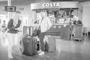 Zwei Frauen vor mehreren Gepäckstücken mit einem Kaffee in der Nähe, wahrscheinlich am Flughafen.