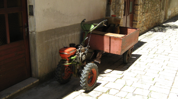 Ein Traktor mit Anhänger auf einer Straße neben einem Haus mit Türen.