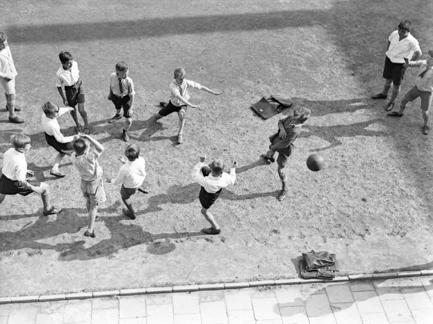 Eine Gruppe junger Jungs, die Fußball auf einem Feld in Schwarz-Weiß spielen, tragen Shorts und Schuhe und haben Taschen auf dem Boden um sie herum.