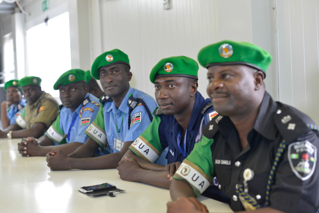 Gruppe von Polizeibeamten sitzt an einem Tisch während einer Schulung, mit Mobiltelefonen und anderen Gegenständen auf dem Tisch, in einem Raum mit Fenstern und Deckenlampen.