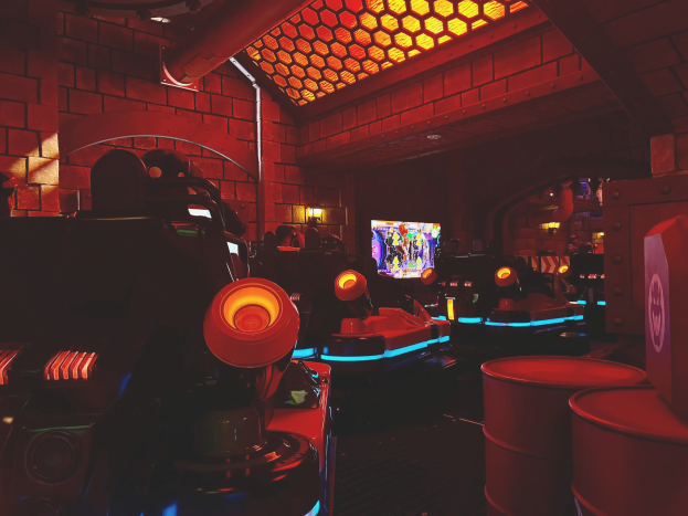 Ein hell erleuchteter Arcade-Raum voller verschiedener Videospielautomaten, Bildschirme und Gegenstände, einschließlich einer sichtbaren Röhre und Deckenleuchten.