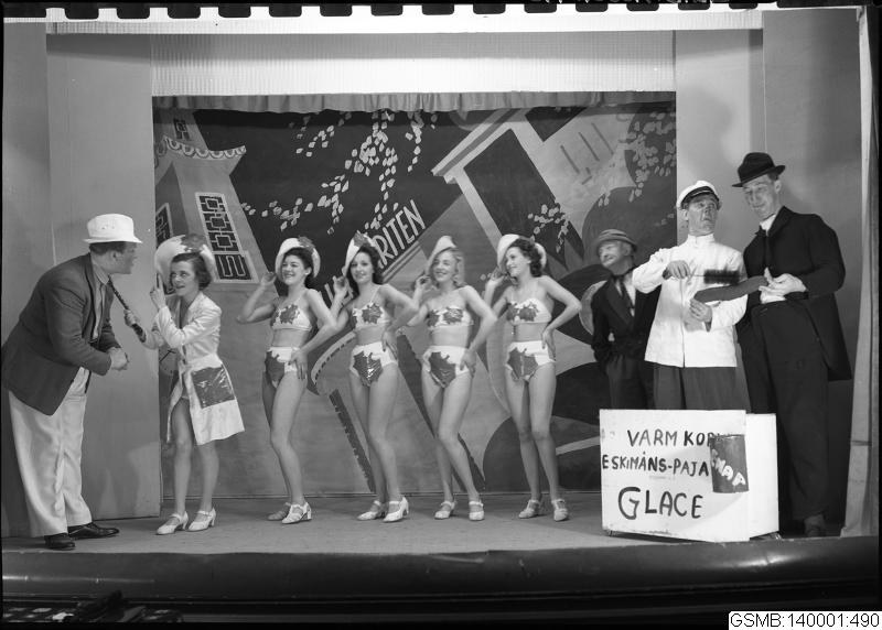 Black and white photo of a group of competition winners on a stage holding objects, with a board and wall in the background.