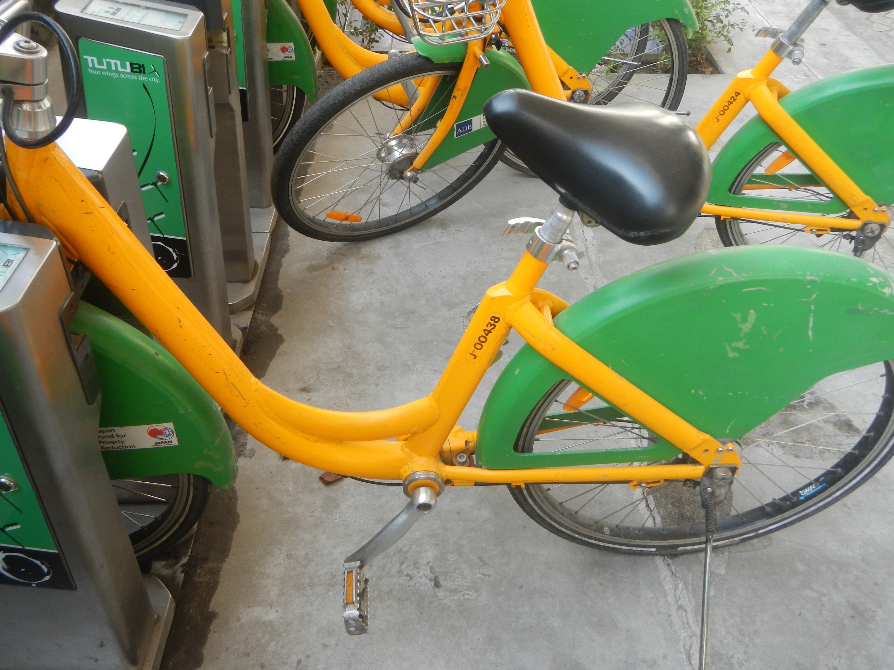 Eine Reihe gelber und grüner Fahrräder, die nebeneinander geparkt sind, mit Maschinen links und Pflanzen im Hintergrund.