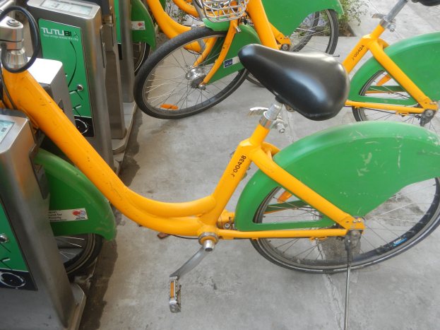 Eine Reihe gelber und grüner Fahrräder, die nebeneinander geparkt sind, mit Maschinen links und Pflanzen im Hintergrund.