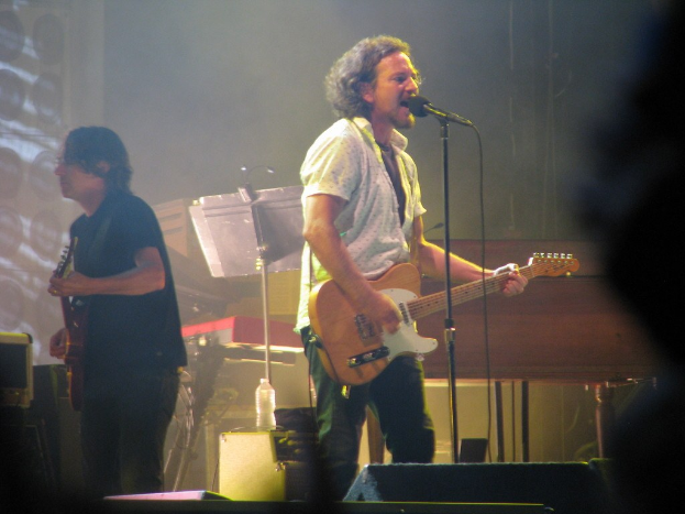Paul McCartney performing on the Tonight Show Starring Jimmy Fallon, playing guitar while wearing a blazer and tie, with musical instruments and a "Beatles" sign visible behind him.