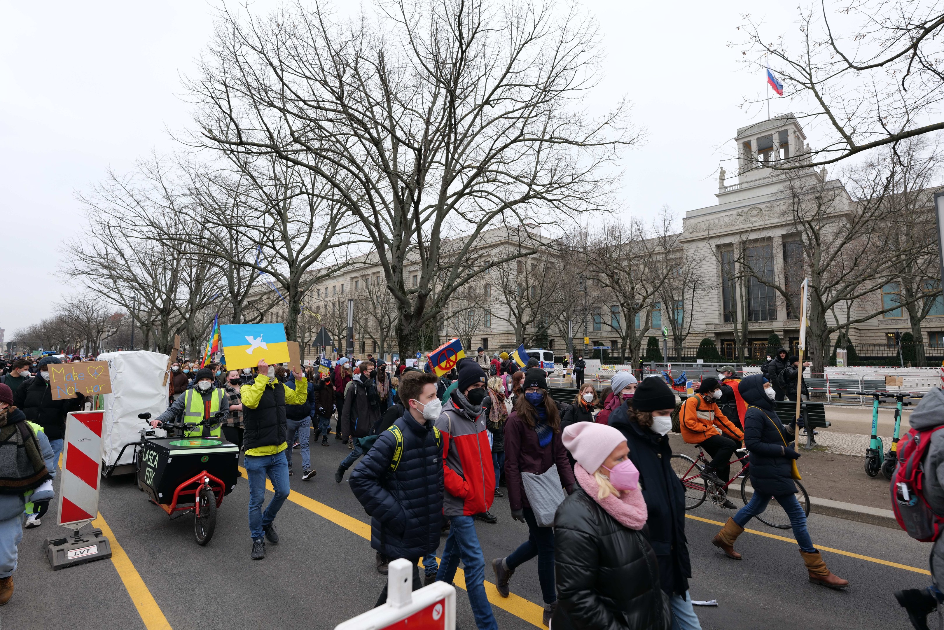 Eine große Gruppe von Menschen marschiert bei einer Demonstration auf einer Straße, einige halten Schilder und andere fahren Fahrräder, mit Bäumen, Straßenschildern und einem Gebäude im Hintergrund unter einem klaren blauen Himmel in Washington, D.C. am 21. Januar 2020.